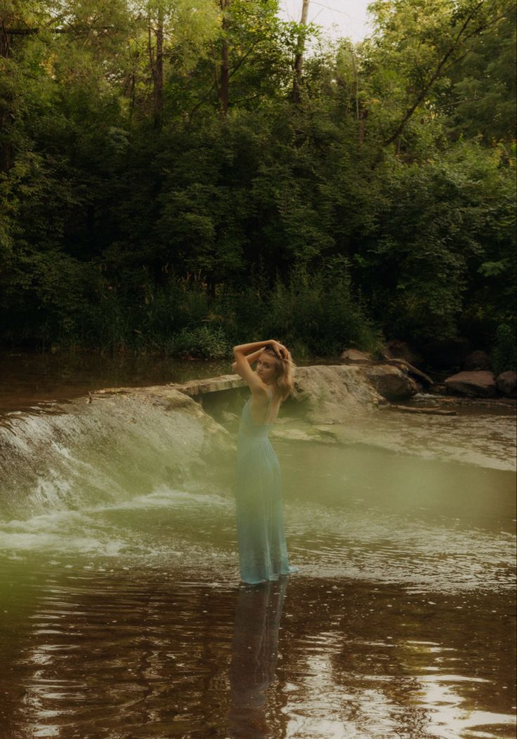 a woman is standing in the water with her hands on her head and arms behind her head