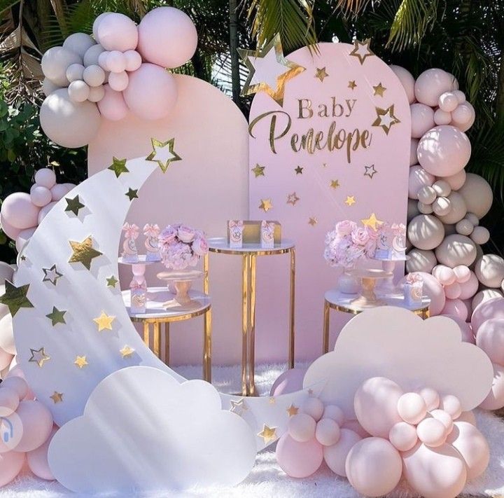 a pink and gold baby shower with balloons, stars and clouds on the ground next to a sign