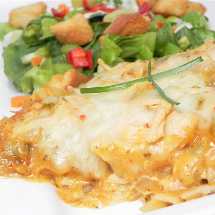 a white plate topped with lasagna covered in cheese and sauce next to a salad