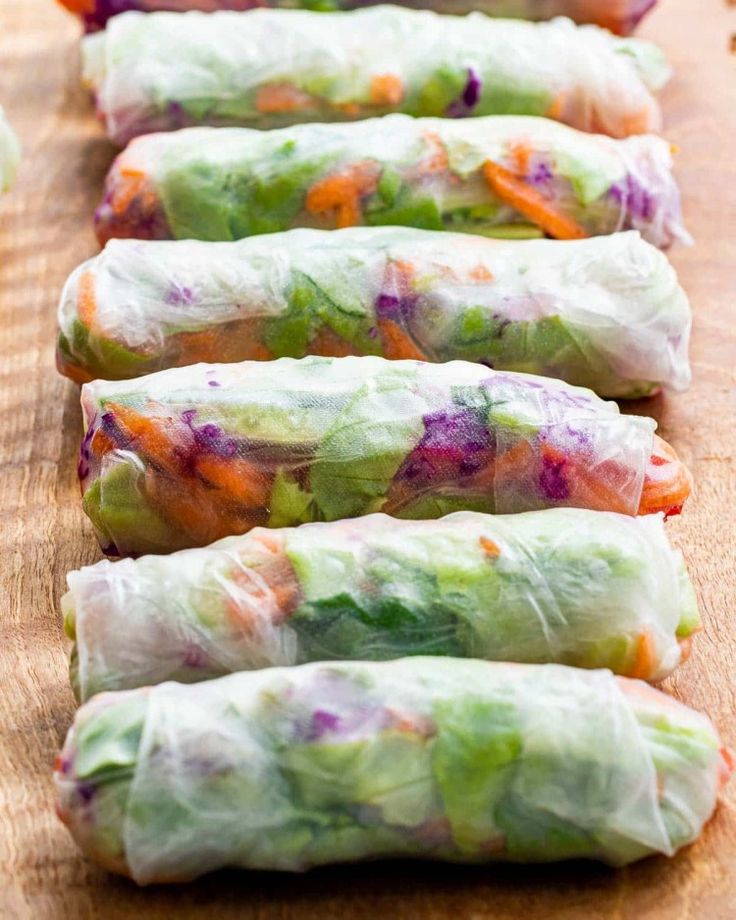 four rolls filled with vegetables sitting on top of a wooden cutting board