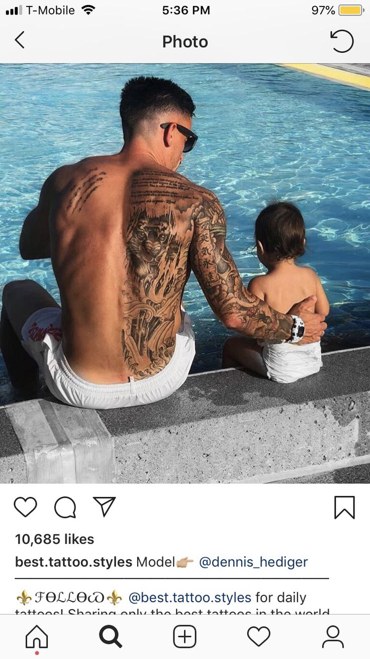 a man with tattoos sitting next to a little boy near a pool and looking at the water