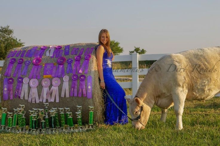 a woman standing next to a cow in a field with bottles on it's back