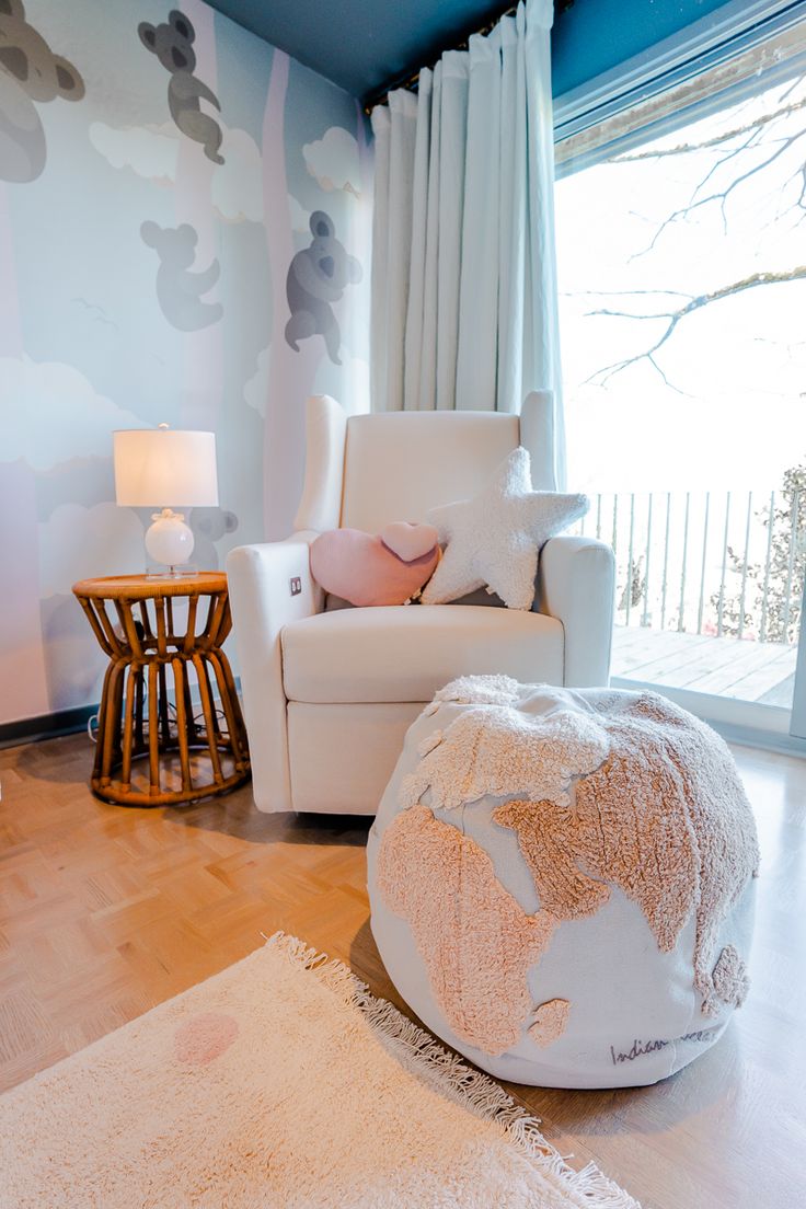 a living room with a white chair and large round ottoman in front of a window