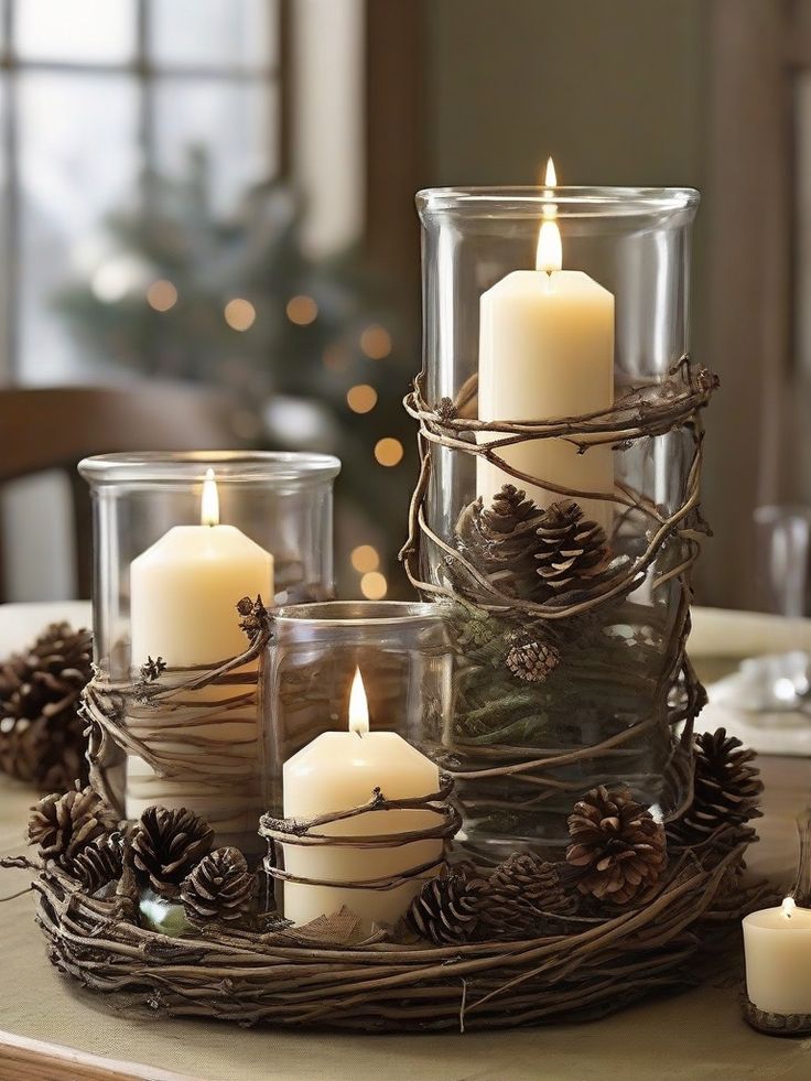 some candles are sitting on a table with pine cones and branches around them in glass containers