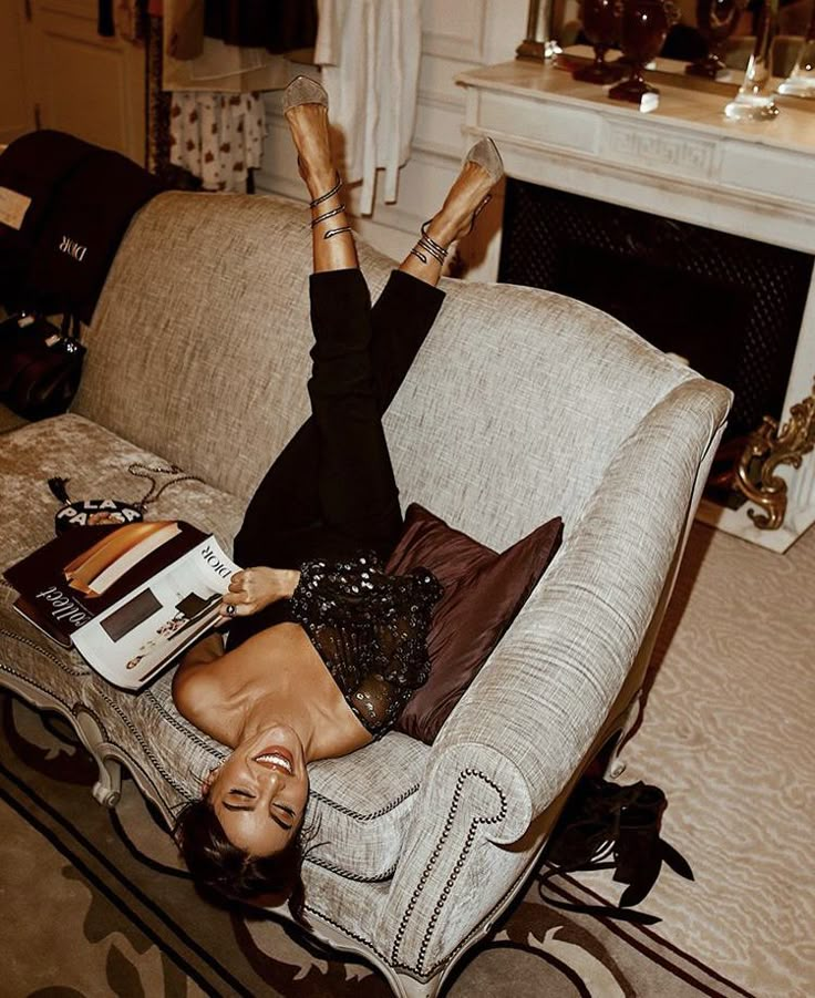 a woman laying on top of a couch with her legs up in the air while reading a book