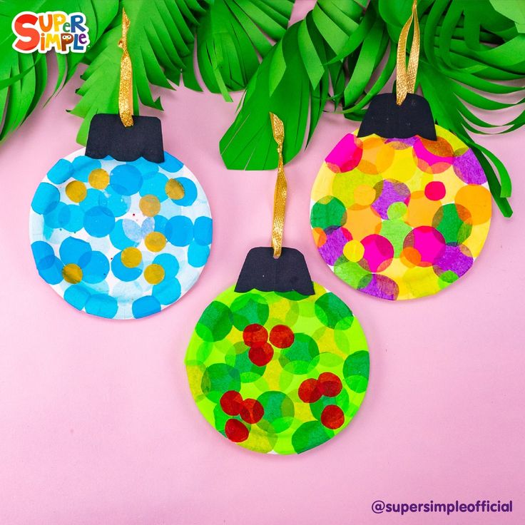 three paper plate christmas ornaments hanging from a tree branch on a pink background with green leaves