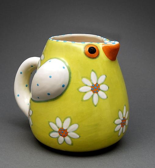 a yellow and white bird shaped vase with daisies on it's side, sitting on a gray surface