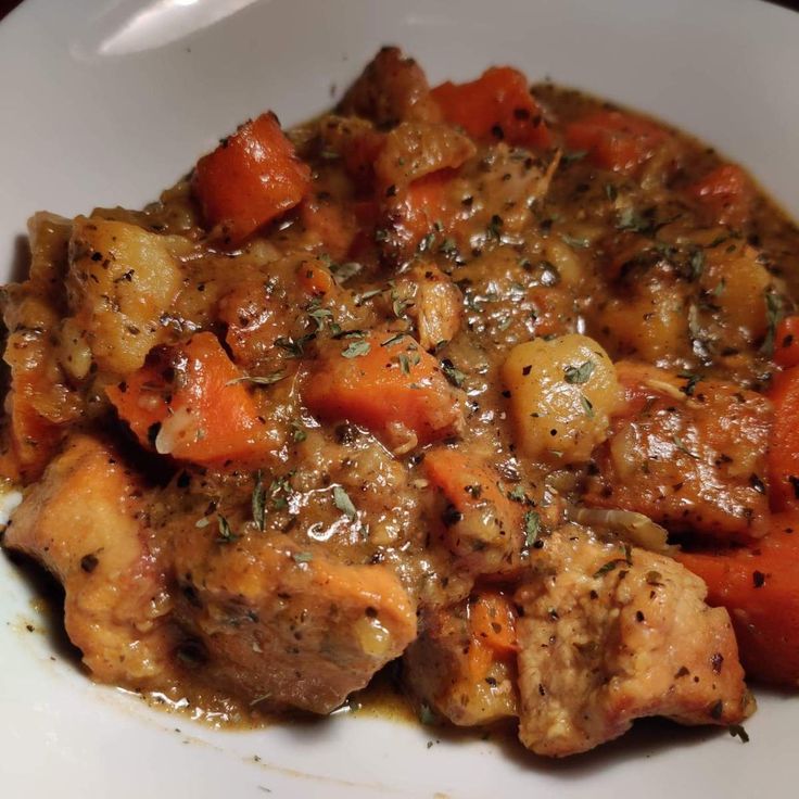 a white plate topped with meat and carrots covered in gravy on top of a wooden table