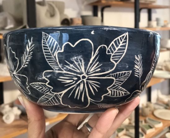 a hand holding up a blue bowl with white flowers on it in front of shelves