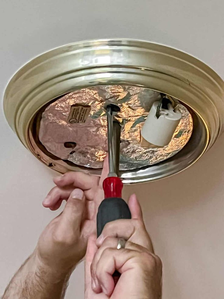 a person is fixing a light fixture with a screwdriver and an air conditioner