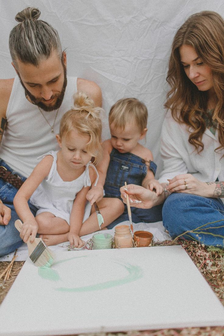 a man, woman and two children are sitting on the ground painting with paintbrushes