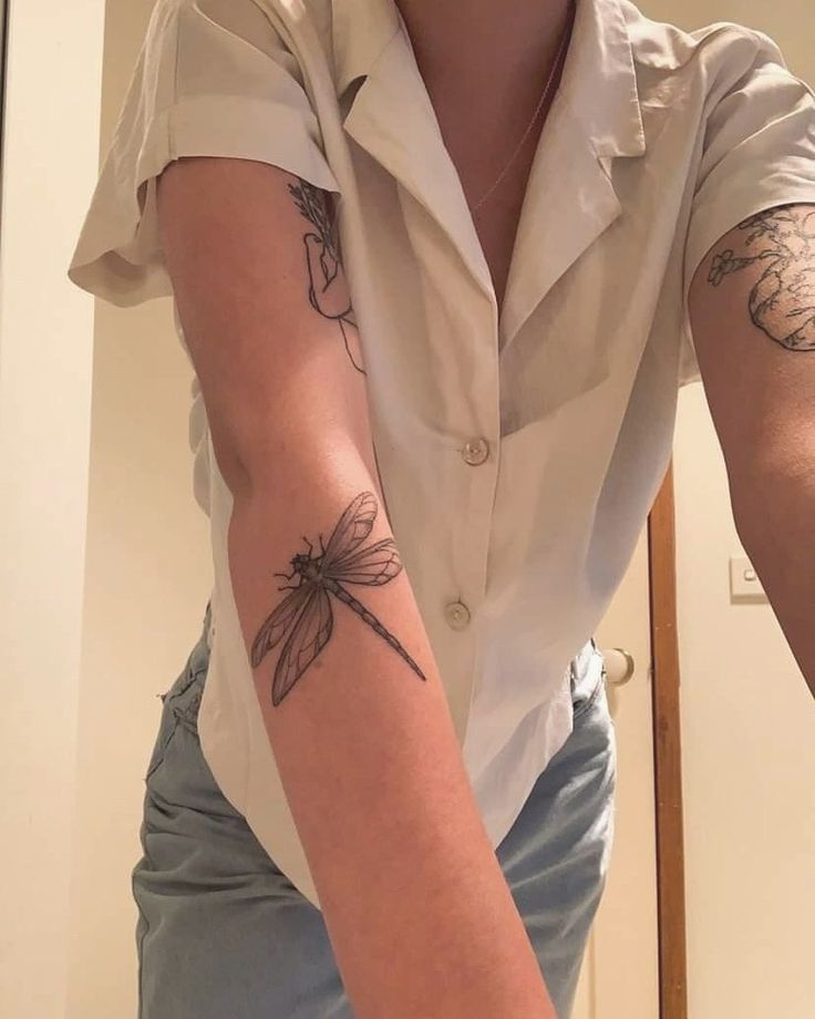 a woman with a dragonfly tattoo on her arm is taking a selfie in the mirror