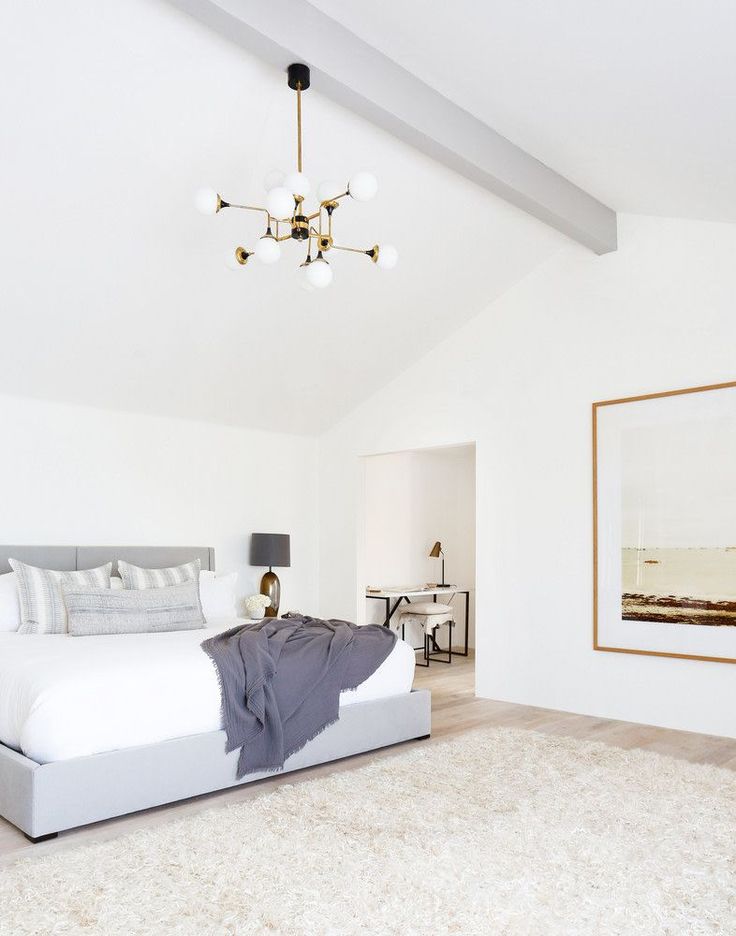 a white bedroom with a large bed and chandelier hanging from it's ceiling