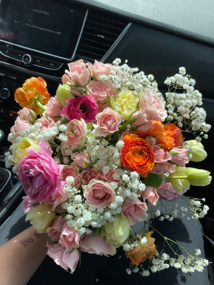 a bouquet of flowers sitting in the center of a car dash board with someone's hand holding it