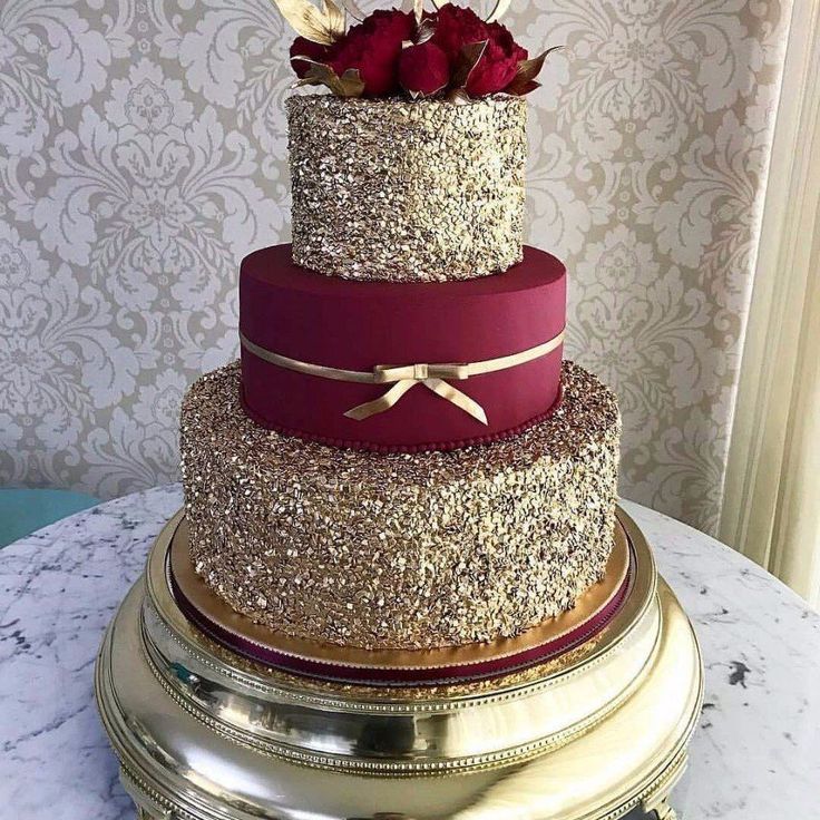 a three tiered wedding cake with red roses on top and gold trimmings