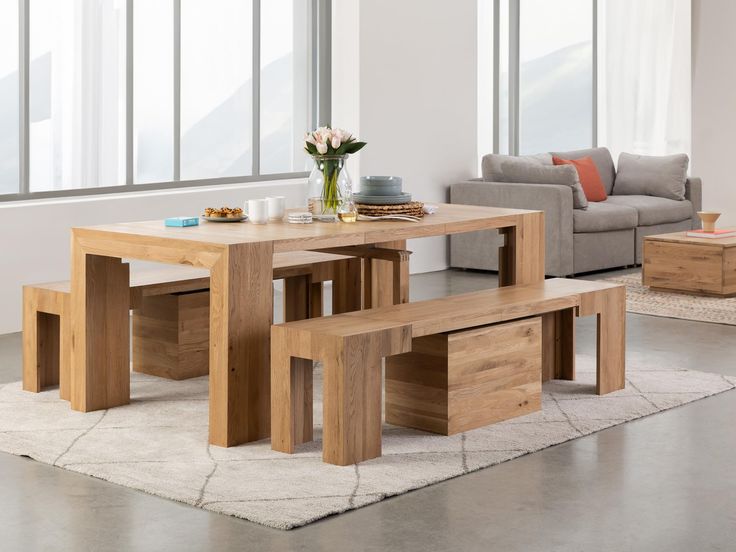 a wooden table and benches in a room with large windows, rugs and couches