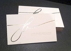 two white business cards with black ink on them sitting on a table next to each other