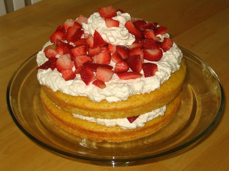 a cake with strawberries on top sitting on a glass plate next to a wooden table