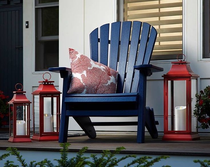 a blue chair sitting on top of a porch next to two lanterns and a red pillow