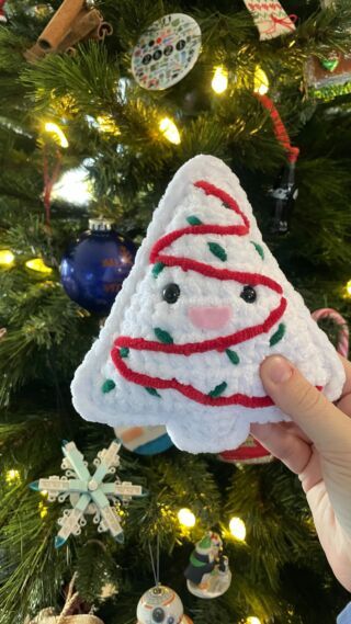 someone is holding up a crocheted christmas tree ornament in front of a decorated christmas tree