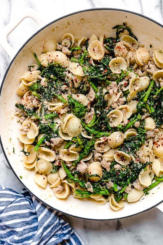 a pan filled with pasta and broccoli on top of a marble countertop