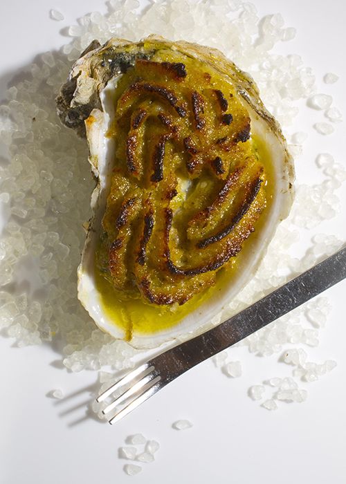 an open oyster on top of sea salt next to a fork and knife with mustard