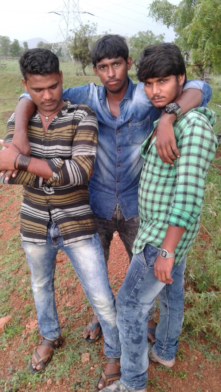 three young men standing next to each other on a dirt road with trees in the background