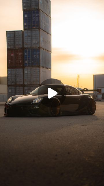 a black sports car parked in front of a tall building with shipping containers on it