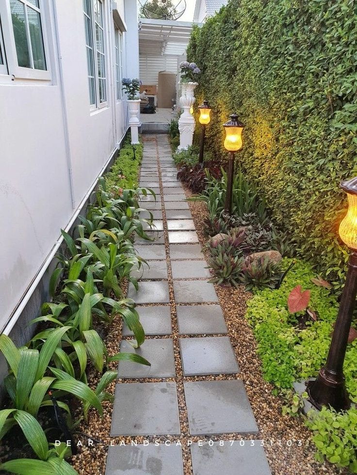 a walkway between two houses with plants and lights on either side, leading to the front door