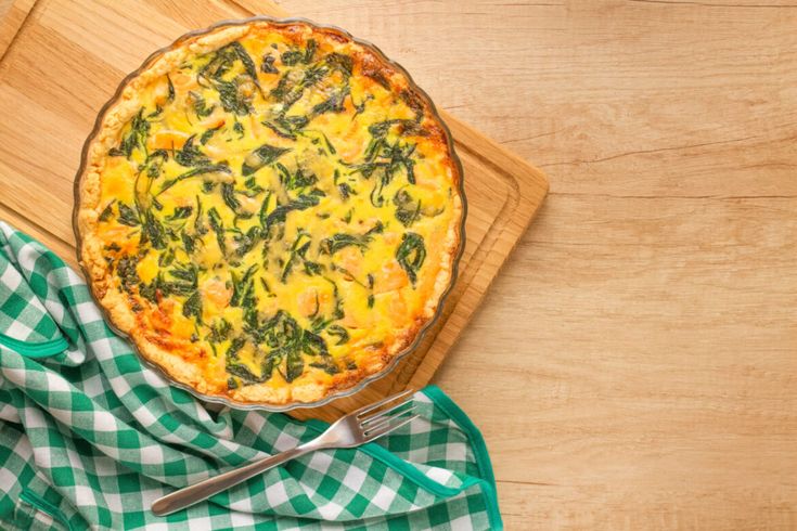 a quiche with spinach and cheese on a cutting board next to a fork