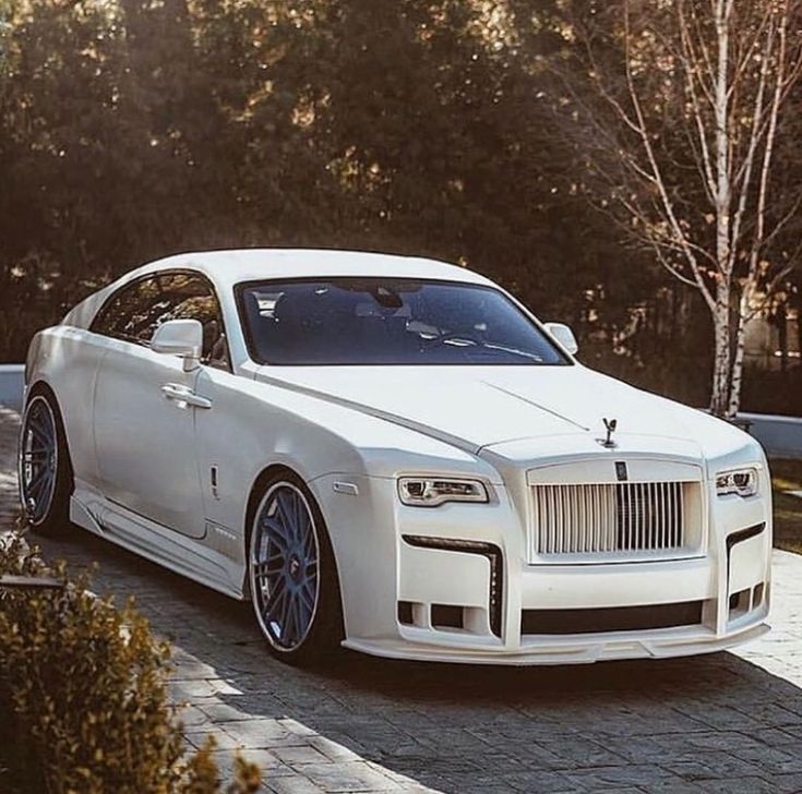 a white rolls royce parked in front of some trees