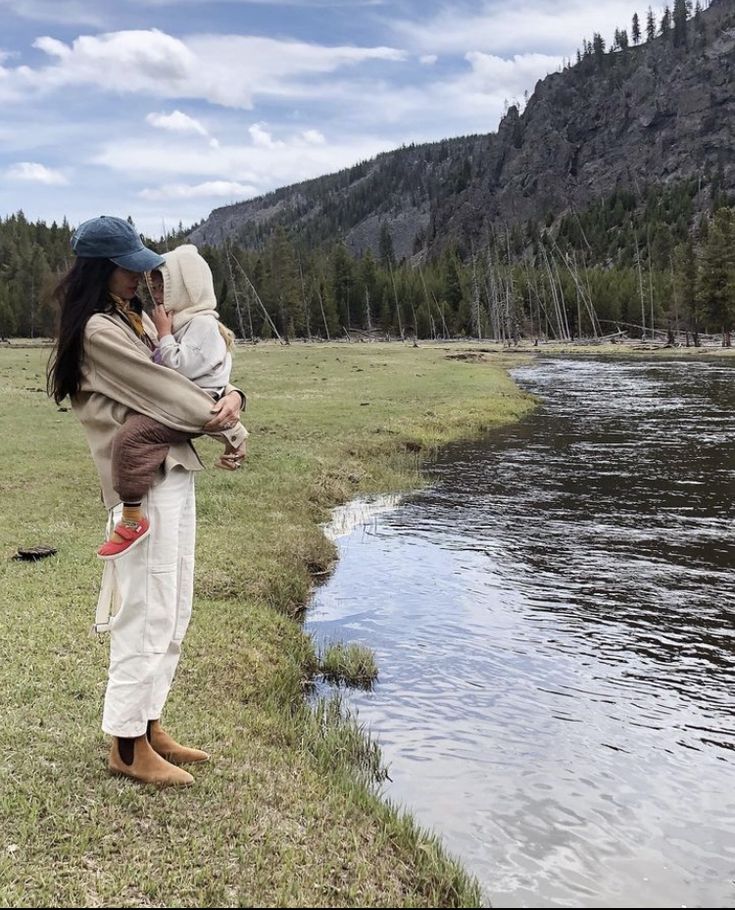 a woman holding a baby standing next to a river