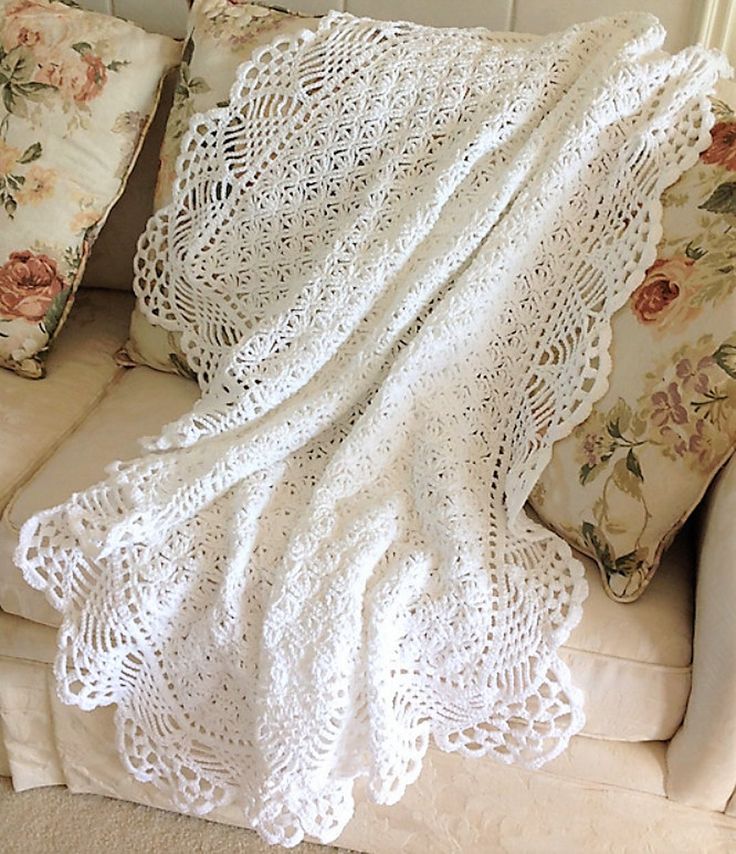 a white crocheted blanket sitting on top of a couch next to two pillows