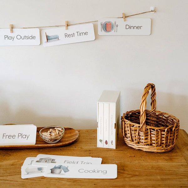 a wooden table topped with books and baskets filled with food next to cards that read play outside, rest time dinner