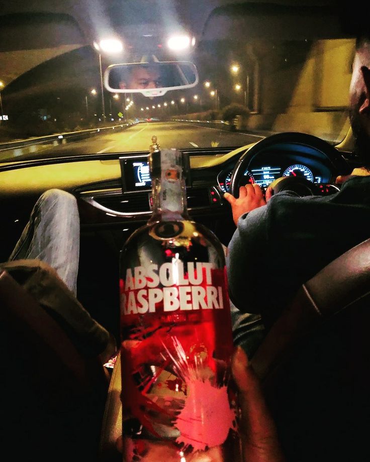 a man sitting in the back seat of a car holding a bottle of absolut raspberry