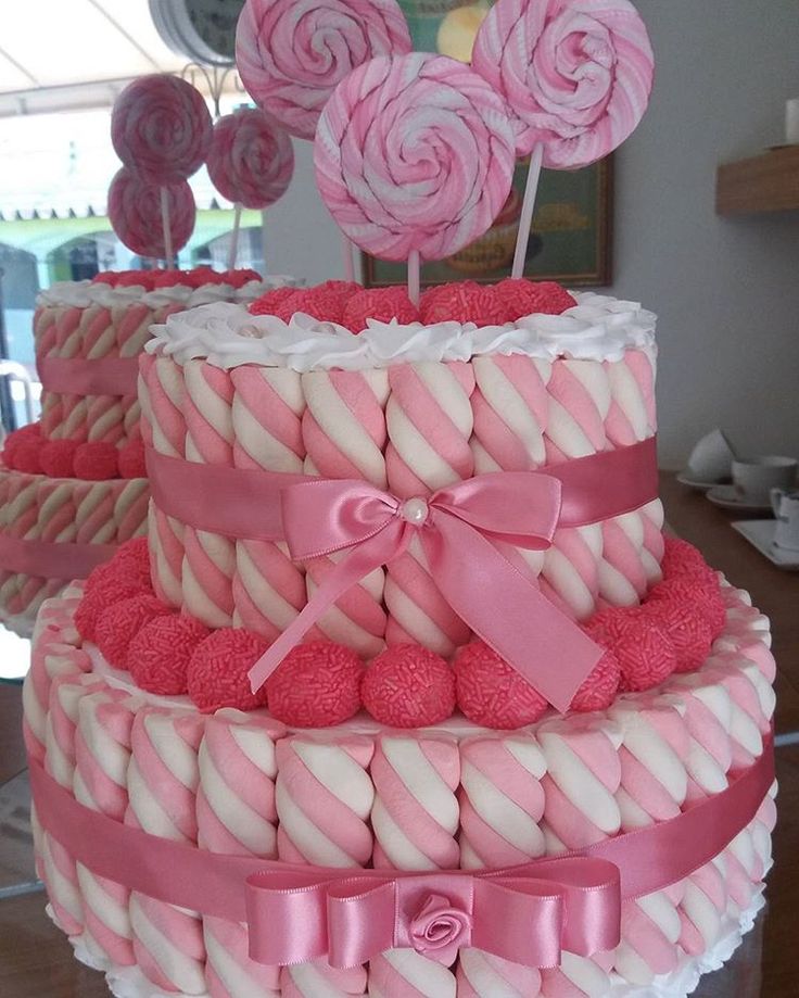 a three tiered cake decorated with pink and white lollipops