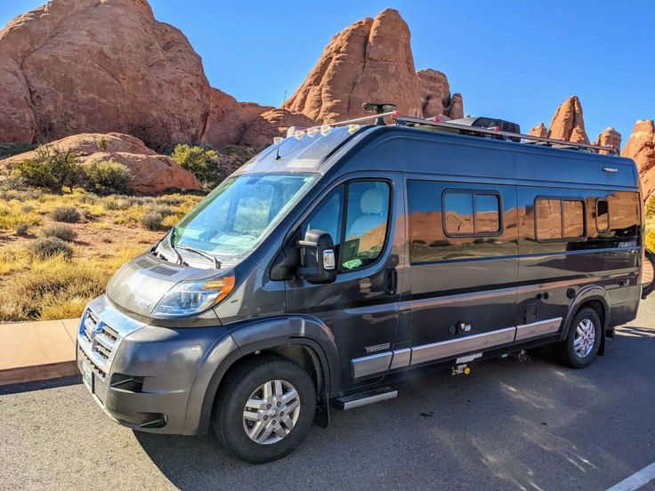 an rv is parked in front of some large rocks and desert like area with mountains