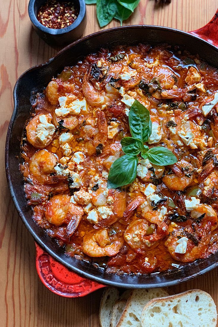 a skillet filled with shrimp and cheese on top of a wooden table next to bread