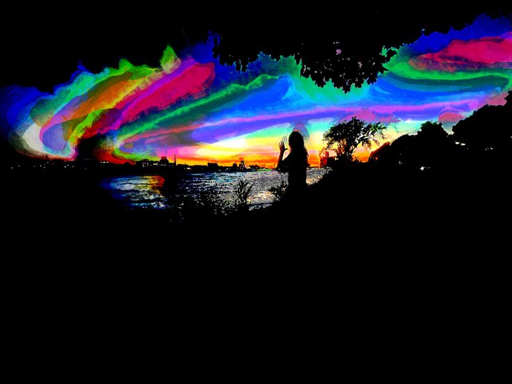 the silhouette of a person standing in front of a lake with colorful clouds above them