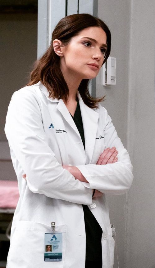 a woman in a white lab coat standing with her arms crossed and looking off to the side