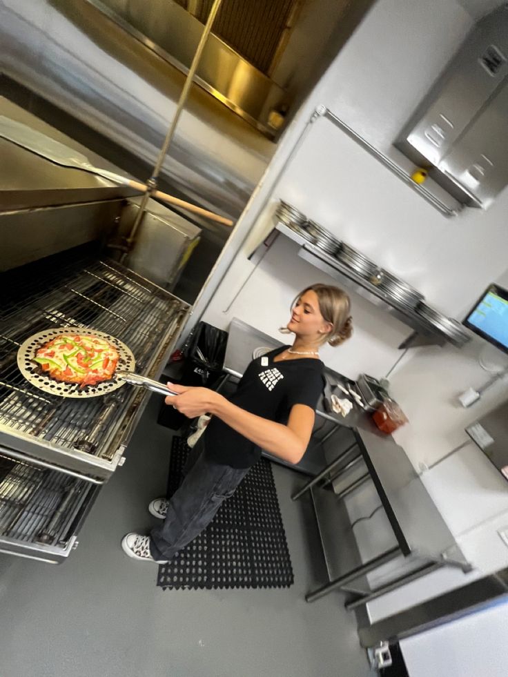 a woman standing in front of an oven with a pizza on the rack next to her