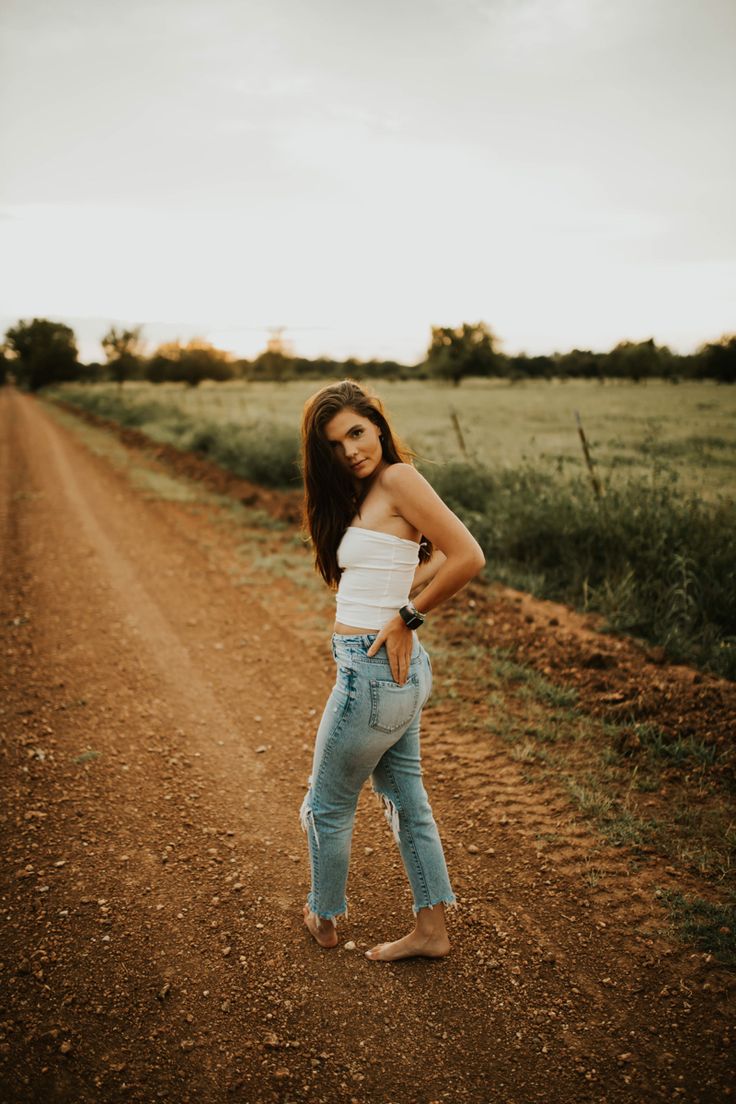 a woman standing in the middle of a dirt road with her hands on her hips