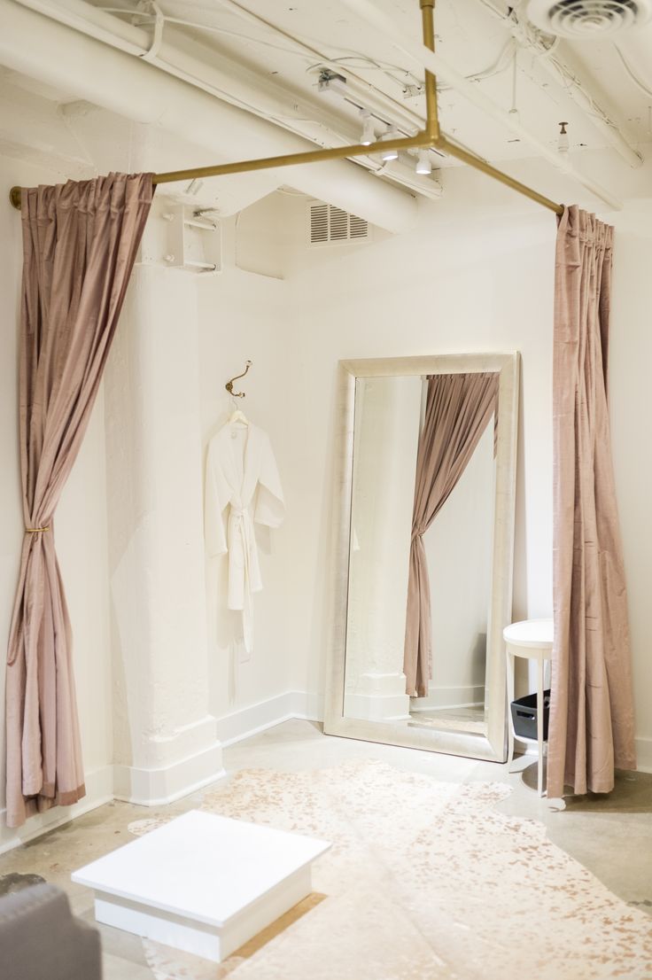 a white room with pink curtains and a large mirror on the wall next to it