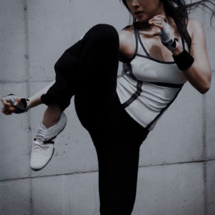 a woman in white shirt and black pants doing a dance move with one foot on the ground