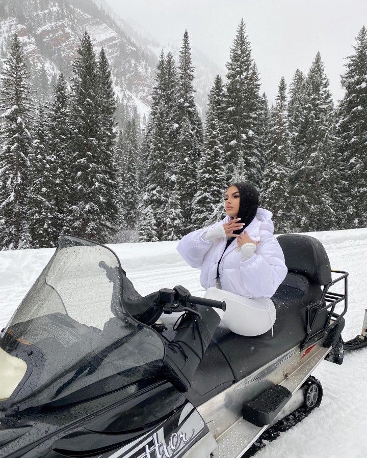 a woman sitting on top of a snowmobile in front of some trees and snow