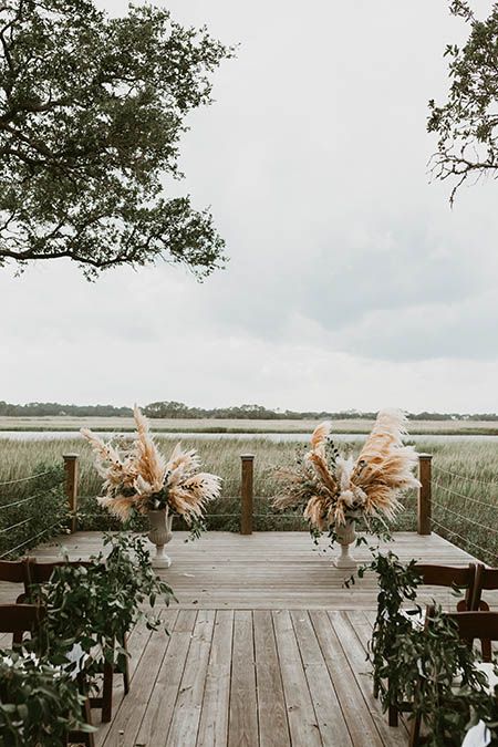 an outdoor ceremony setup with chairs and flowers in vases on the side of a wooden deck