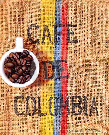 coffee beans in a small white bowl sitting on top of a burlock with the word cafe de colombia painted on it