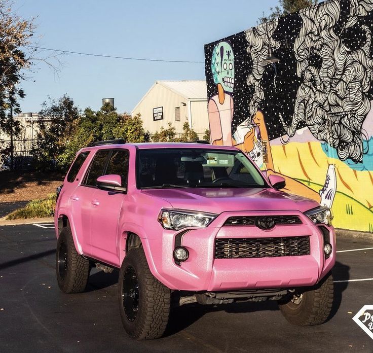 a pink toyota truck parked in front of a graffiti covered wall with the word hello kitty painted on it