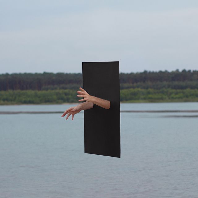 a hand reaching out from behind a black piece of paper in the air over a body of water