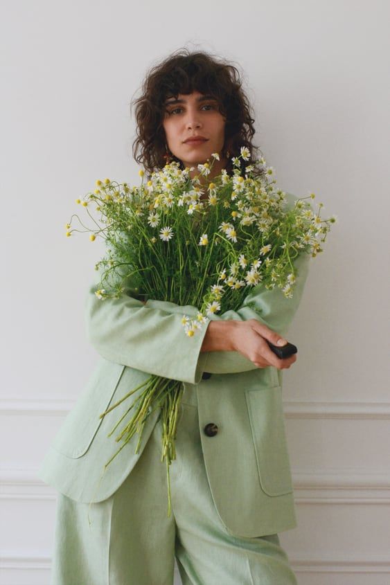 a woman holding flowers in her hands and wearing a green suit with buttons on the front